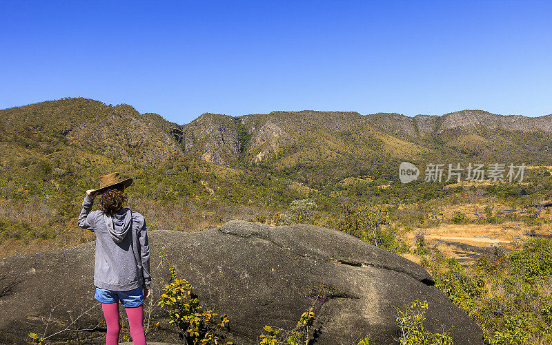 小女孩戴着牛仔帽站在一块岩石上观看Chapada dos Veadeiros的风景